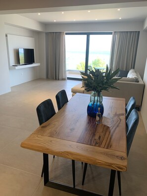 Un salon moderne avec une table à manger en bois, des chaises noires, un canapé et un téléviseur fixé au mur.