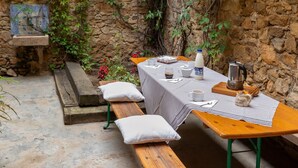 Un espace de restauration en plein air agrémenté d’un mur en pierre, de bancs en bois et d’une table dressée pour deux personnes.