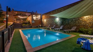 Une piscine avec un mur en pierre et un espace patio couvert.
