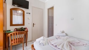 Ein Hotelzimmer mit Bett, Schreibtisch mit Stuhl, Wandfernseher und einer Tür zum Badezimmer.