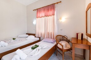Una habitación con dos camas individuales, una silla de madera, un escritorio y una ventana con cortinas.