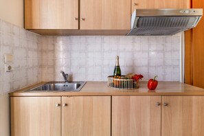 Una cocina con un lavamanos de acero inoxidable, armarios de madera, una campana extractora empotrada y una cesta de frutas con un pimiento rojo.