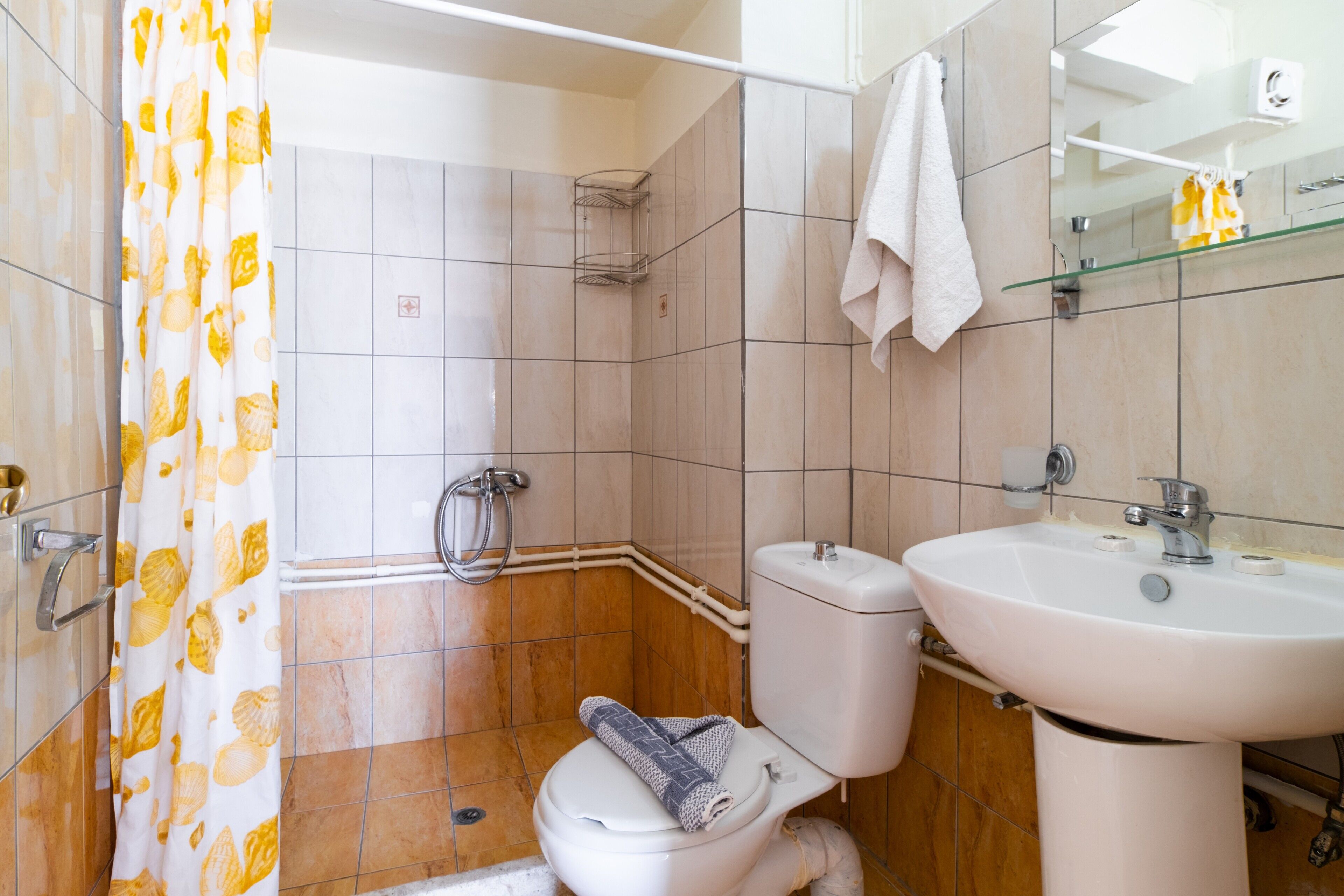 A bathroom with a toilet, sink, shower, and a towel hanging on the wall.