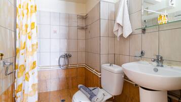 A bathroom with a toilet, sink, shower, and a towel hanging on the wall.