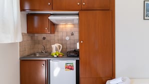 A compact kitchen with wooden cabinets, a built-in stove, a refrigerator, and a sink. - Nikiana Club - Studio 3 Apartment with Sea View & Wi-Fi (Lefkada)
