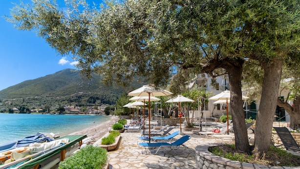 A stone-paved beach area with lounge chairs and umbrellas, boats, and a view of the sea and mountains. - Nikiana Club - Studio 3 Apartment with Sea View & Wi-Fi (Lefkada)
