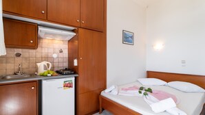 A compact room with a kitchenette, a bed with pillows, and a small wall-mounted light. - Nikiana Club - Studio 3 Apartment with Sea View & Wi-Fi (Lefkada)