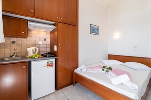 A compact room with a kitchenette, a bed with pillows, and a small wall-mounted light.