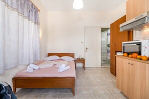A bedroom with a bed, a bedside table, a wardrobe, and a kitchenette area.