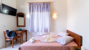A bedroom with a bed, a desk, a chair, a television, and a window with curtains. - Apartment-Studio "Nikiana Club - Studio 2" with Sea View & Wi-Fi (Lefkada)