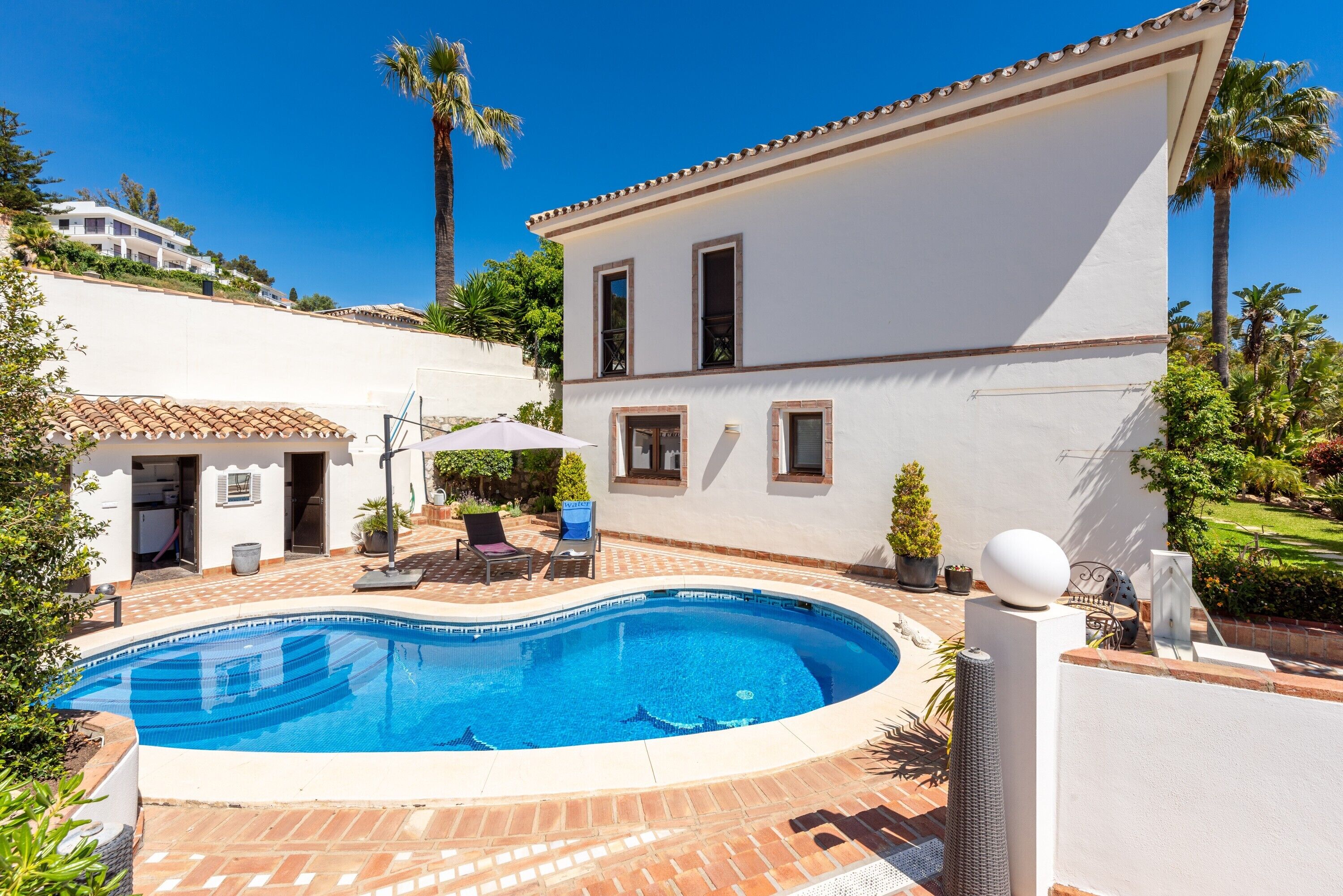Una piscina, un patio con sedie e un edificio bianco con tetto in tegole.