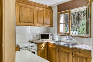 A kitchen with wooden cabinets, a microwave, a sink, and a window with a view of trees.