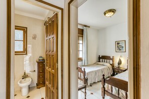 Ein Schlafzimmer mit einem hölzernen Bett, einem Nachttisch, einem Fenster mit Vorhängen und einem an der Wand hängenden Kunstwerk.