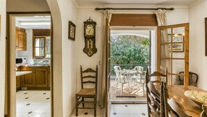 A room with a wooden dining table, a chair, a clock, and a view of a balcony with outdoor furniture. - Holiday Home 'Villa Montgó Parc Con Piscina' with Mountain View, Shared Pool and Air Conditioning (L'Escala)