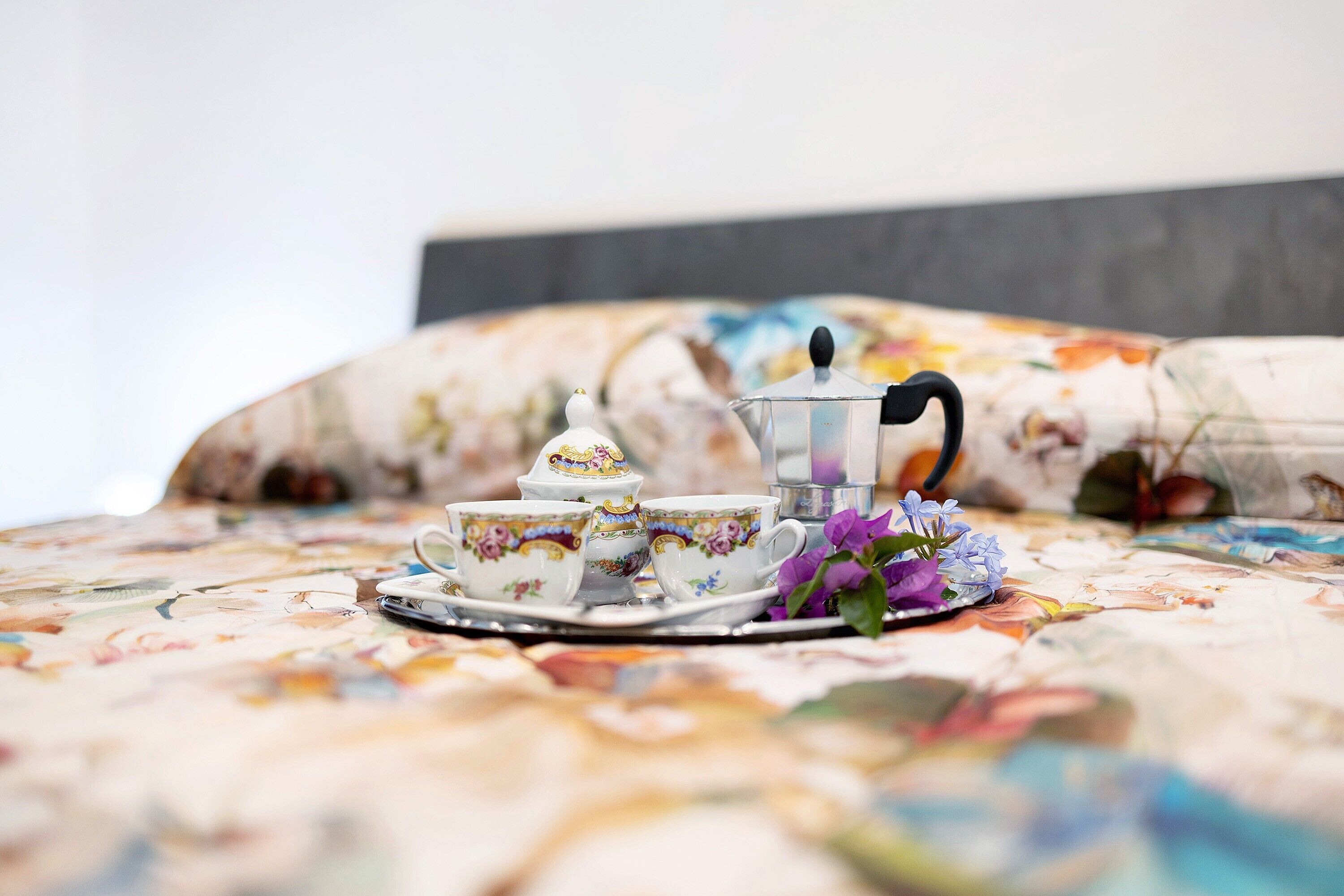 A bed with floral bedding, a tea set, and a floral arrangement.