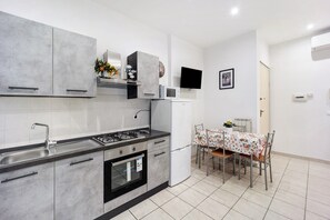 Une cuisine moderne équipée d’une cuisinière à gaz, d’un four, d’un réfrigérateur et d’un four à micro-ondes. On y trouve une table à manger avec des chaises et un téléviseur fixé au mur.