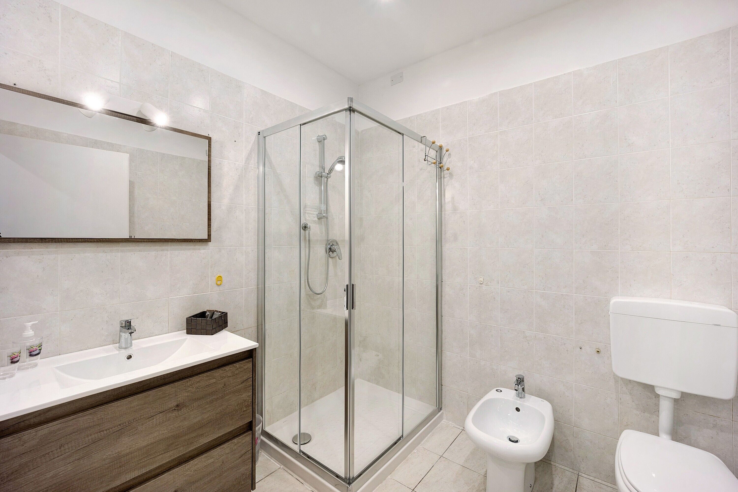 Een moderne badkamer met een douche met glazen wand, een wastafel met spiegel en een toilet.