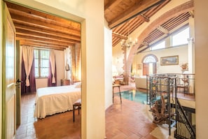 A room with a bed, a chair, a window with curtains, a wooden ceiling, and a staircase leading to a balcony. - Villa "Il Fornacino" with Pool, Garden & Wi-Fi (Rapolano Terme)