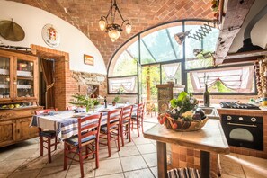 A rustic kitchen with a brick ceiling, wooden cabinets, a dining table with chairs, and a large window with curtains. - Villa "Il Fornacino" with Pool, Garden & Wi-Fi (Rapolano Terme)