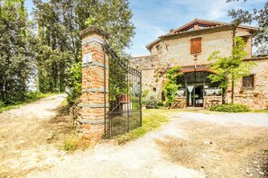 A rustic stone building with a brick entrance gate, a paved driveway, and a restaurant with outdoor seating. - Villa "Il Fornacino" with Pool, Garden & Wi-Fi (Rapolano Terme)