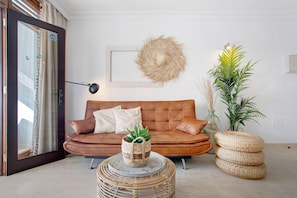 Une pièce avec un canapé en cuir marron, une table basse ronde en osier, une plante en pot et un luminaire fixé au mur.