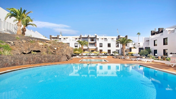 Ein Pool mit Liegestühlen, eine felsige Landschaft und Gebäude mit Balkonen.