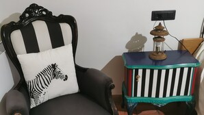 Een zwarte fauteuil met een zebra kussen, een bijzettafeltje met een lamp en een betegelde vloer.