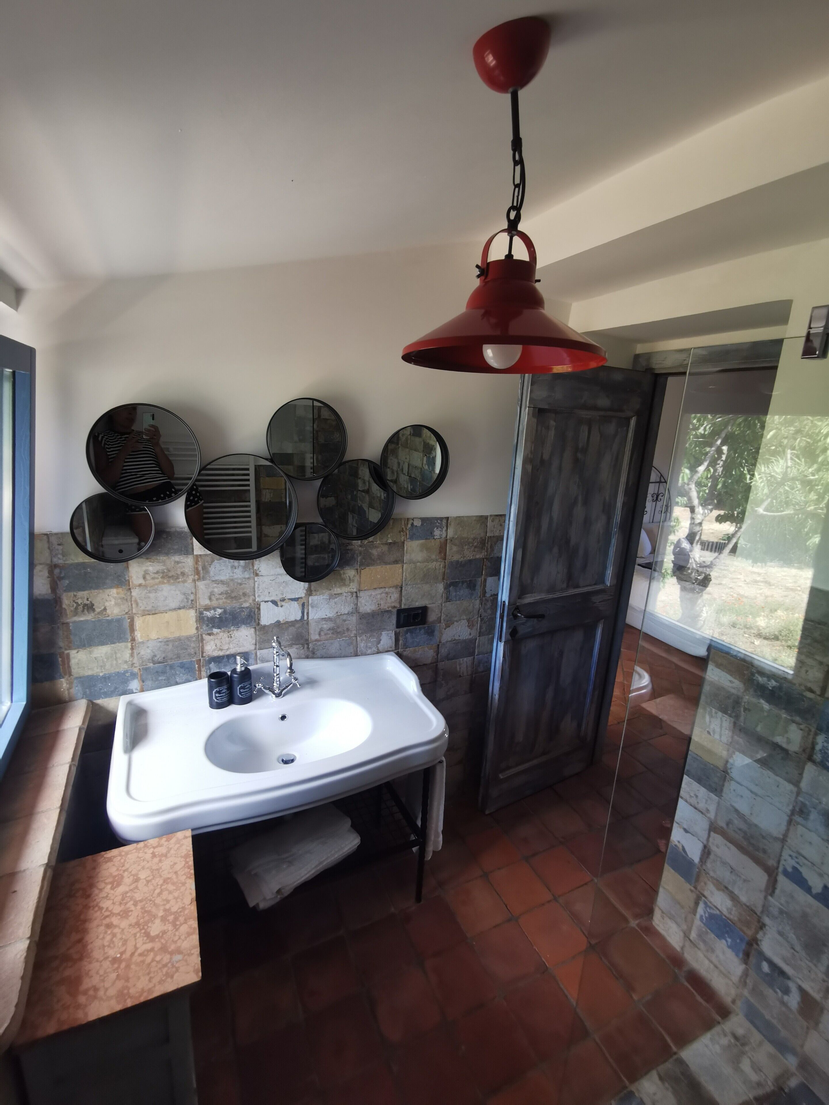 Une salle de bain avec un lavabo blanc, un luminaire suspendu rouge et plusieurs miroirs ronds accrochés au mur.