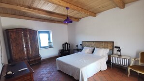 Een slaapkamer met een houten plafond, een bed met wit beddengoed, een houten garderobe, een klein raam en een stoel.