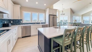 A modern kitchen with a central island, stainless steel appliances, and a dining area with green chairs. - Make Lasting Memories at 'Memory Maker' | Pool, Hot Tub, Game Room | Perfect for Large Families (Corolla)