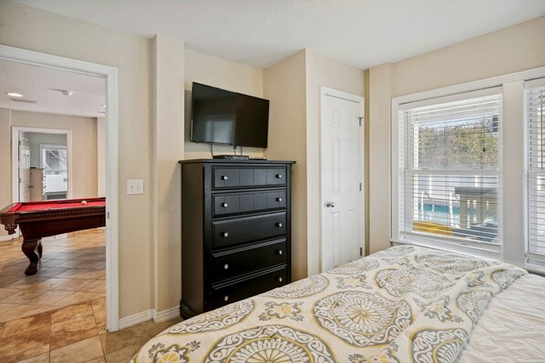 A bedroom with a bed, a dresser, a television, and a pool table in the adjacent room. - Make Lasting Memories at 'Memory Maker' | Pool, Hot Tub, Game Room | Perfect for Large Families (Corolla)