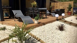 Una terrazza esterna con un pavimento in legno, poltrone relax, un tavolo e piante in vaso.