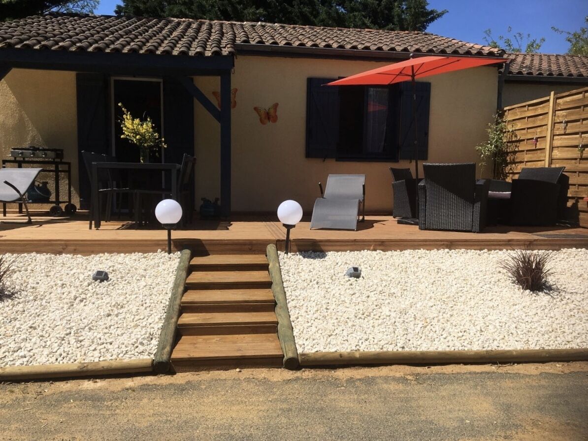 A patio area with a table and chairs, a barbecue grill, and a red umbrella.