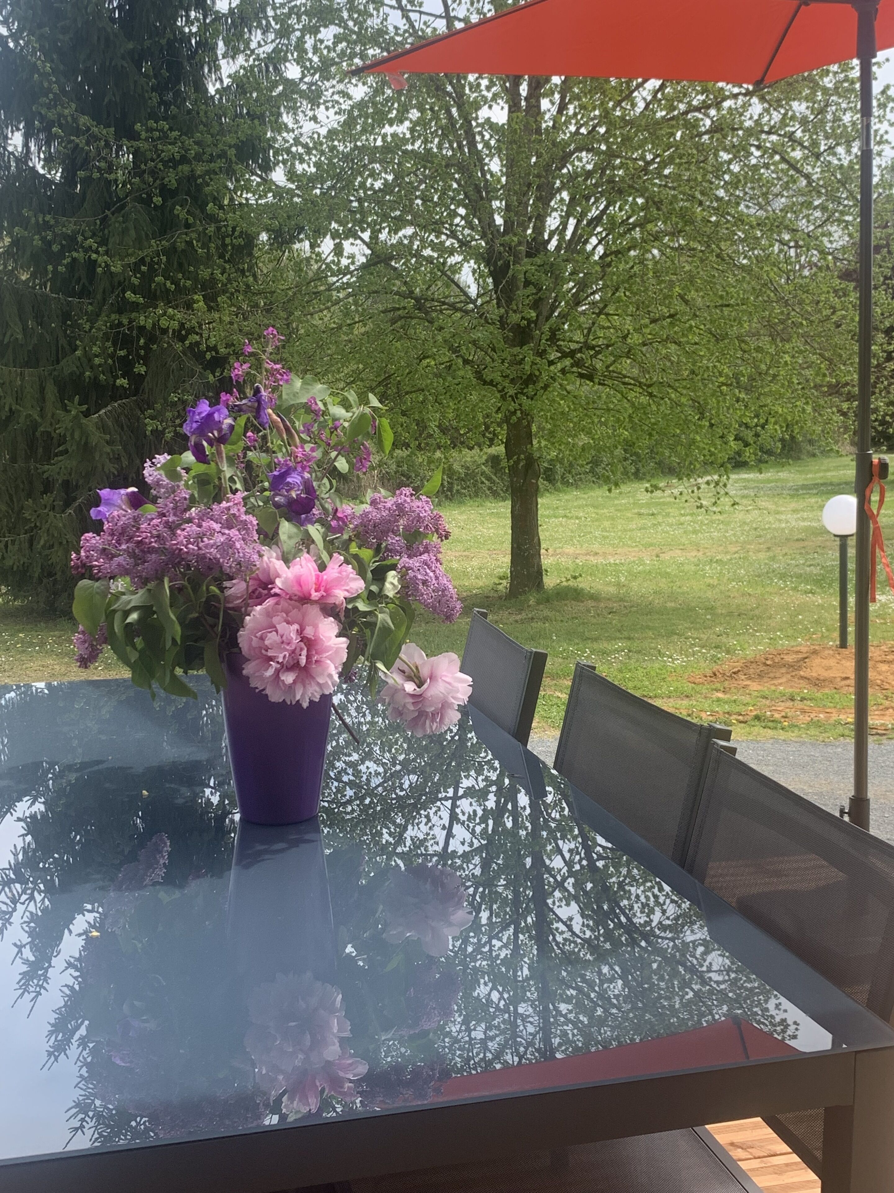 Una mesa con cubierta de vidrio y un florero morado lleno de flores.
