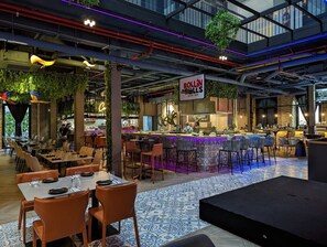Un restaurante moderno con barra, techos altos con tuberías a la vista y una variedad de arreglos de asientos.