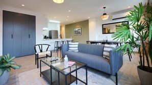 Ein modernes Wohnzimmer mit einer Couch, Sesseln, einem Glastisch und einer Essecke mit Tisch und Stühlen.