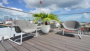Ein Balkon mit zwei Korbstühlen, einer Topfpflanze und Blick auf die Stadt.