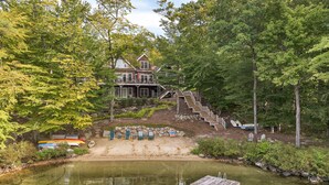 A lakeside property with a dock, a sandy beach, and a staircase leading to a house. - 5000 SF Winnipesaukee Luxury For 14 With 455 Feet Waterfront (Moultonborough)