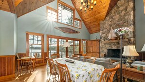 A spacious dining area with a high ceiling and large windows, a stone fireplace, and wooden furniture. - 5000 SF Winnipesaukee Luxury For 14 With 455 Feet Waterfront (Moultonborough)