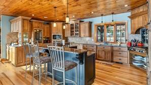 A spacious kitchen with wooden cabinets, a granite countertop, and bar stools. - 5000 SF Winnipesaukee Luxury For 14 With 455 Feet Waterfront (Moultonborough)