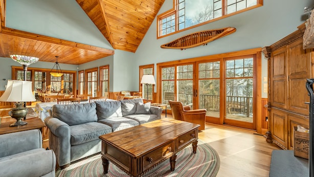 A spacious living room with a high wooden ceiling, large windows, and a cozy fireplace. - 5000 SF Winnipesaukee Luxury For 14 With 455 Feet Waterfront (Moultonborough)