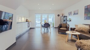 A modern living room with a sofa, coffee table, and a dining area with a table and chairs. There is a kitchen visible in the background. - New Boat Houses (Leirvik)