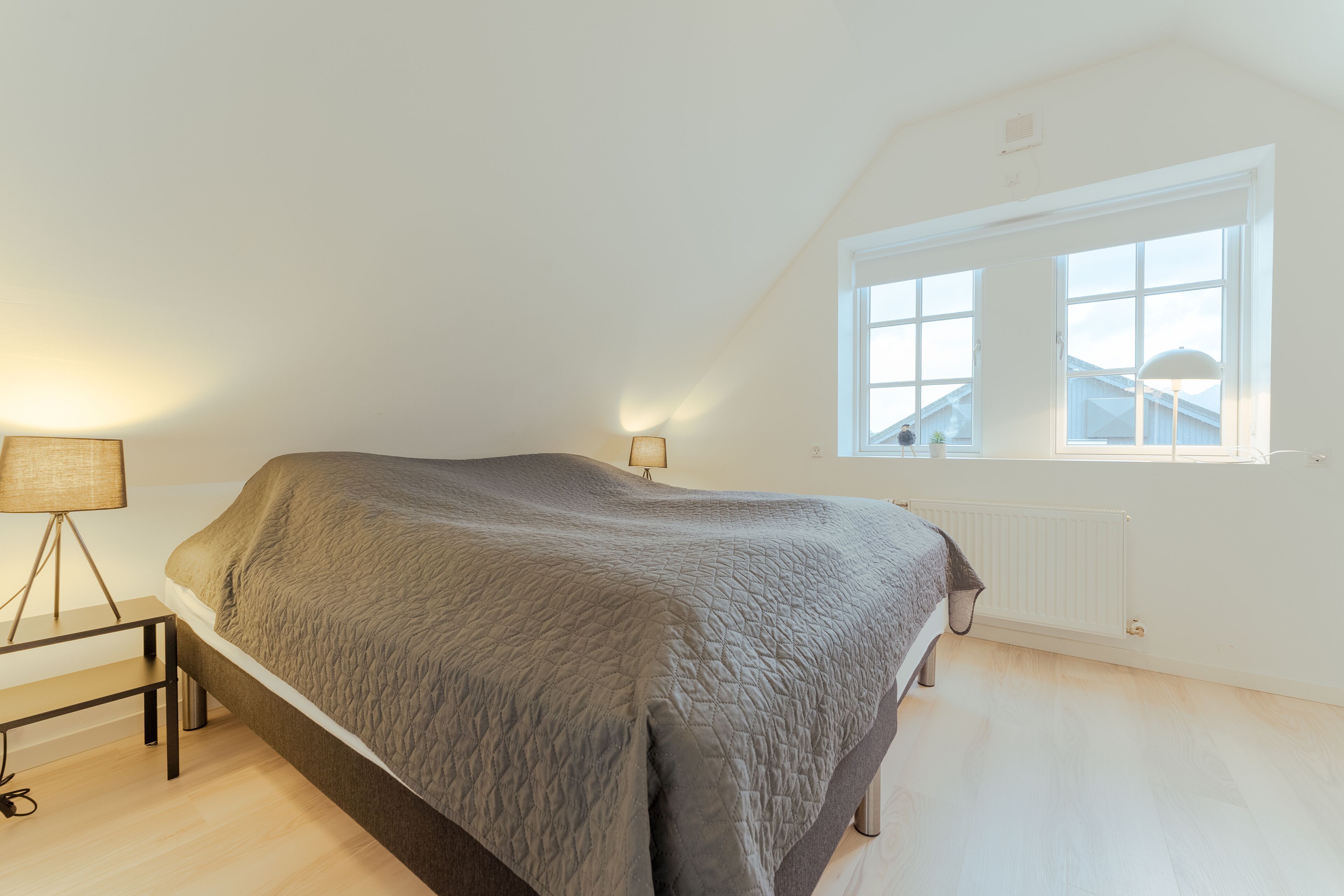 A bedroom with a bed, a bedside lamp, a window, and a radiator.