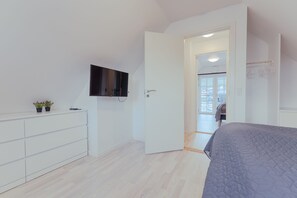 A bedroom with a bed, a TV mounted on the wall, a door leading to another room, and a small plant on the dresser. - New Boat Houses (Leirvik)