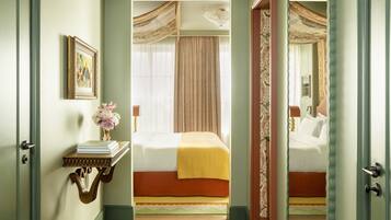 A hallway leading to a bedroom with a bed, a bedside table with a vase, and a mirror on the wall.