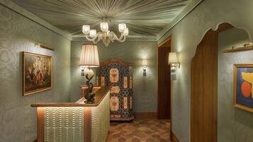 A hallway with patterned wallpaper, a wooden reception desk, a chandelier, and a decorative wall panel.