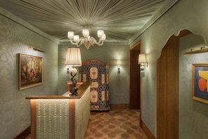 A hallway with patterned wallpaper, a wooden reception desk, a chandelier, and a decorative wall panel.