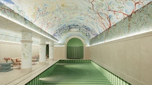 A swimming pool with a green and white striped floor, surrounded by columns and a ceiling with a tree mural. - Hotel Le Grand Mazarin (Paris)