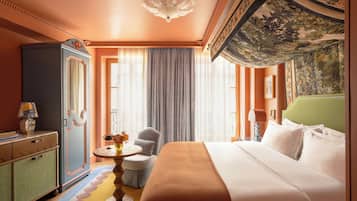 A hotel room with a large bed, a green headboard, a round table with a vase of flowers, a blue wardrobe, and a decorative ceiling.