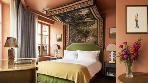 A bedroom with a large bed, a green headboard, a window with curtains, a nightstand with a lamp, and a vase with flowers. - Hotel Le Grand Mazarin (Paris)